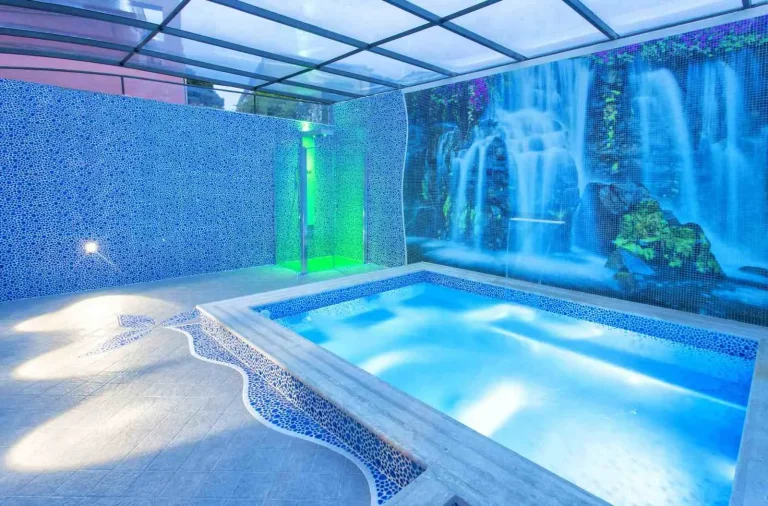 Piscina interna con idromassaggio, cascata e luci, sotto la copertura in vetro